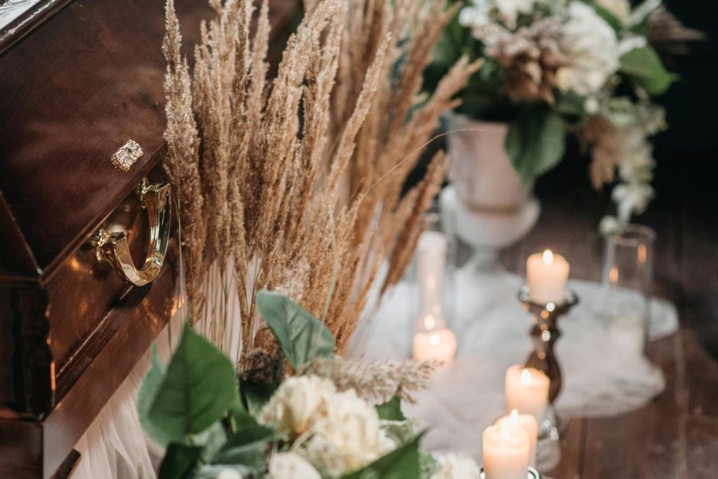 An elegant funeral arrangement with a wooden coffin, flowers, and candlelight indoors.